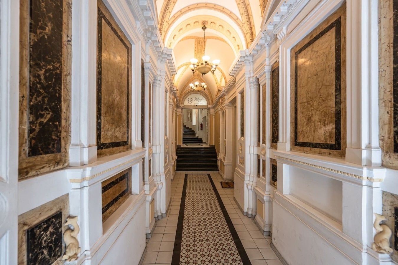 A grand hallway with marble walls, a patterned carpet, and a staircase leading to a higher floor.