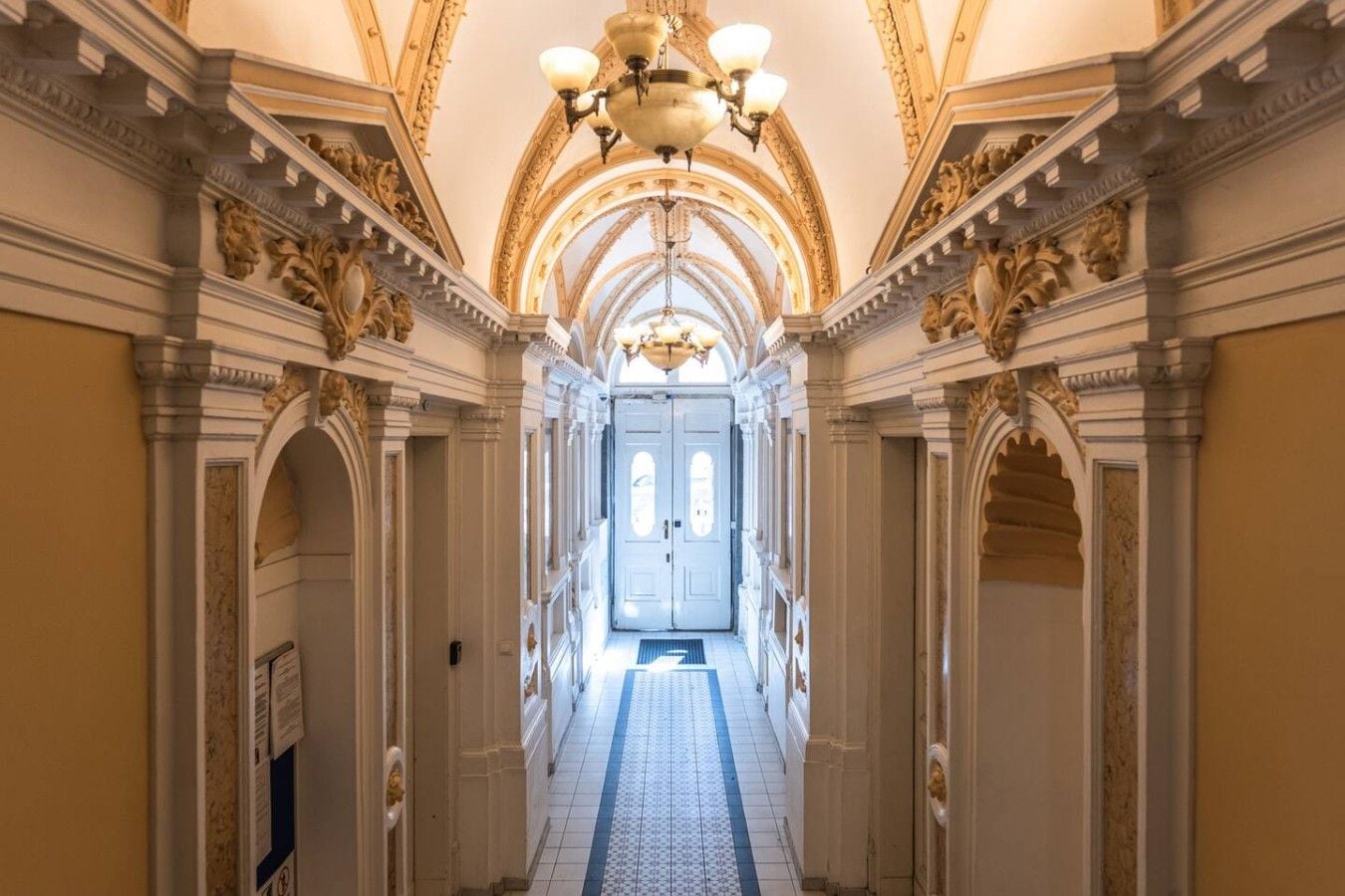 A grand hallway with ornate columns, a chandelier, and a door at the end.