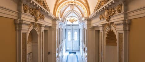 A grand hallway with ornate columns, a chandelier, and a door at the end.