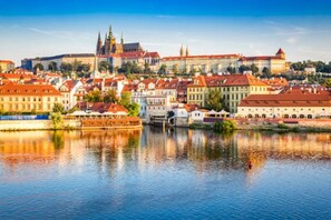 Eine historische Stadtansicht mit einem Fluss, traditioneller Architektur und einer markanten, burgähnlichen Struktur.