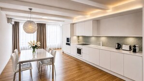 A modern kitchen with white cabinetry, a dining table with chairs, and a pendant light. - Riverside Urban Oasis in Prague’s Coolest District (Prague 8)