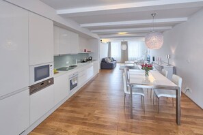 Eine moderne Küche mit weißen Schränken, einem Essbereich mit weißem Tisch und Stühlen sowie einer hängenden Leuchte.
