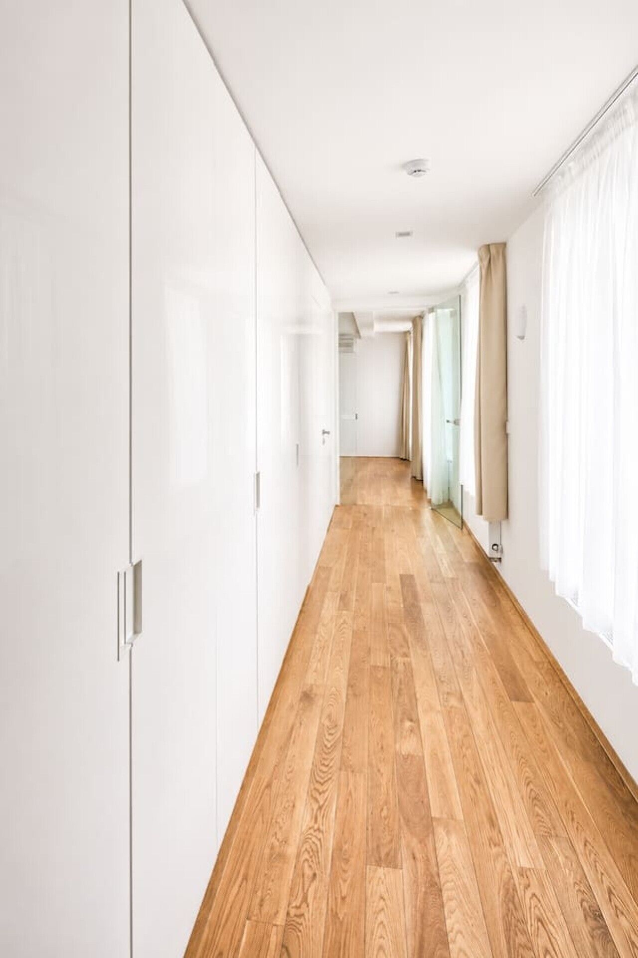 A hallway with wooden flooring, white walls, and a door at the end.