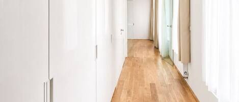A hallway with wooden flooring, white walls, and a door at the end.