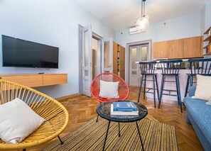 Ein modernes Wohnzimmer mit Flachbildfernseher, Korbstühlen, einem runden Couchtisch und einem Essbereich mit Barhocker.