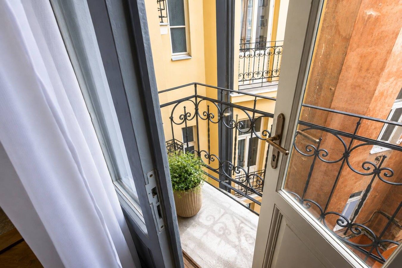 A balcony with wrought iron railings, a potted plant, and a view of adjacent buildings.