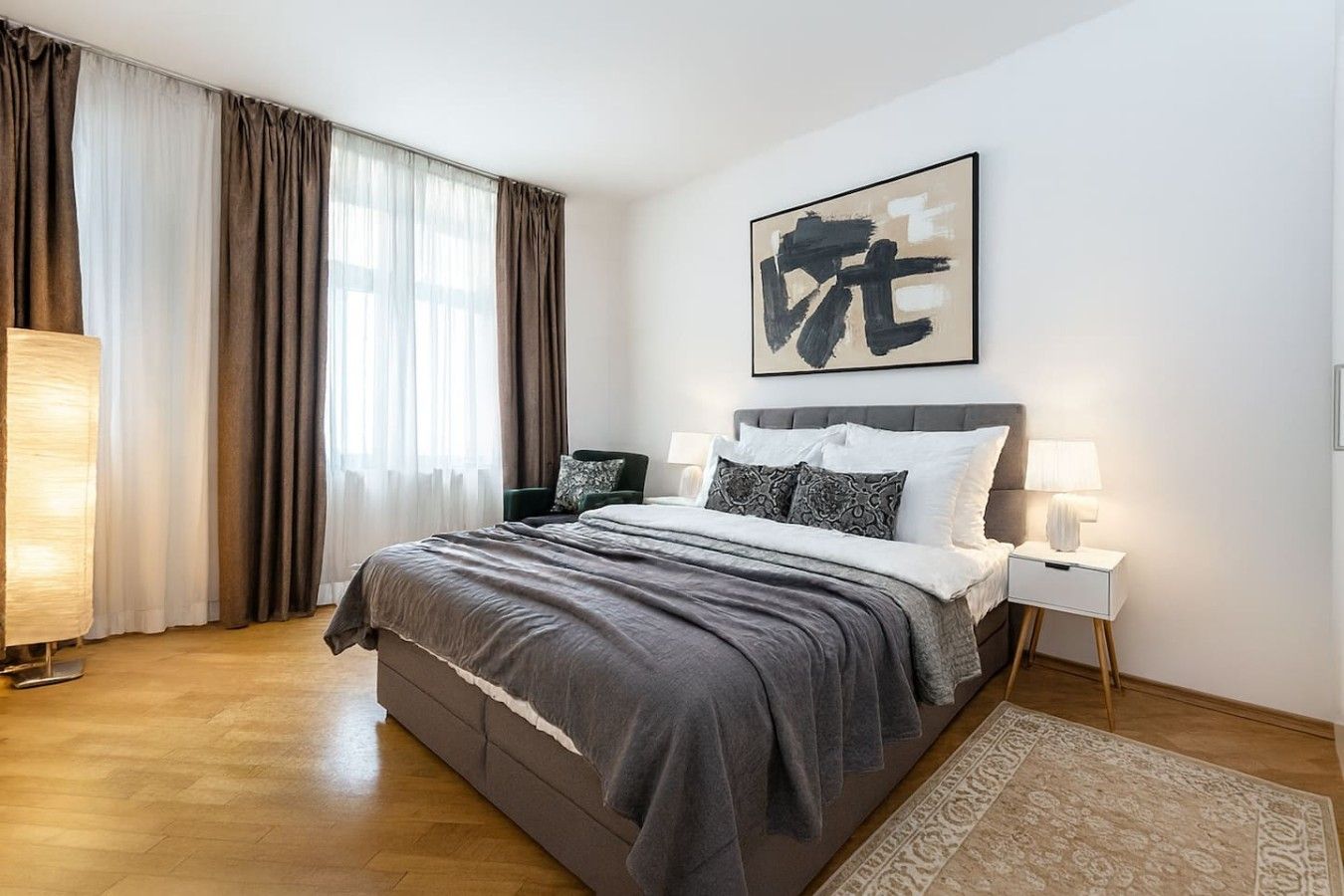 A modern bedroom with a large bed, a bedside table, a lamp, and a window with curtains.