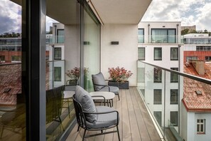 Ein Balkon mit zwei Stühlen, einem Tisch, einer Glastrennwand und Kübelpflanzen.