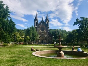 Eine Kirche mit zwei Türmen und einer zentralen Kuppel, umgeben von einem grünen Park mit einem Springbrunnen.