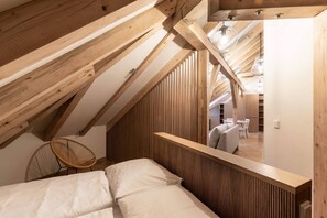 A loft bedroom with wooden beams, a bunk bed, a chair, and a view of the living area. - Elegant Attic Loft in Prime Vinohrady (Prague 2)