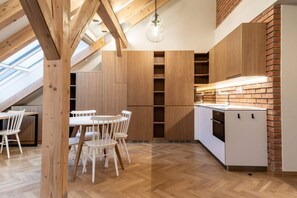 A modern kitchen with wooden cabinets, a dining area with white chairs, and a skylight. - Elegant Attic Loft in Prime Vinohrady (Prague 2)