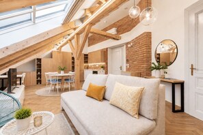 A loft-style room with a high ceiling, exposed wooden beams, a dining area, a sofa with cushions, a small table with a plant, and a mirror on the wall. - Cozy Attic Loft in Prime Location (Prague 2)