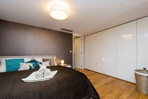 Ein modernes Hotelzimmer mit einem großen Bett, einem Nachttisch, einer Lampe, einem Kleiderschrank und einer Mülltonne.