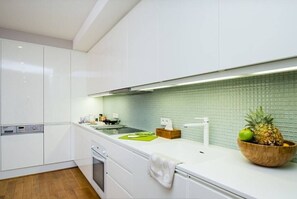 Eine moderne Küche mit weißen Schränken, einer grünen Spritzschutzwand und einer Holzkugel mit Früchten auf der Arbeitsplatte.