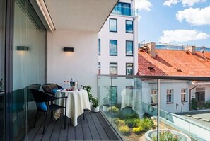 Ein Balkon mit Tisch und Stühlen, einer Glastrennwand und Blick auf Gebäude.