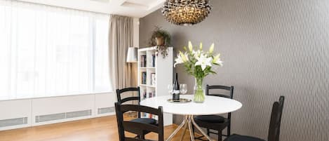 A dining area with a round table, four chairs, a vase of flowers, and a bookshelf.