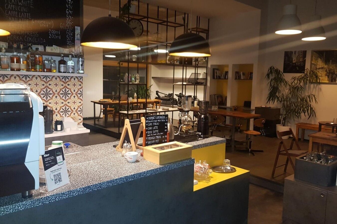 Kahvilan sisustus, jossa on tiskialue, espressokone, istuinalue ja liitutaulusta tehty menutaulu.