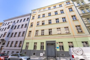A multi-story building with a green and yellow facade, a gray door, and a parked van with 'STOP cafe' on its side. - Top flat close to Wenceslas square with parking (Prague 2)