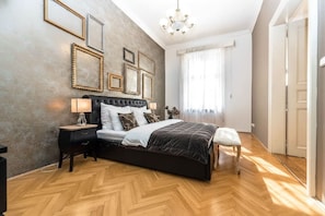 A bedroom with a large bed, a nightstand, a bench, a chandelier, and framed pictures on the wall. - Top flat close to Wenceslas square with parking (Prague 2)