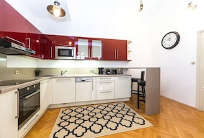 A kitchen with red and white cabinets, a microwave, an oven, a sink, and a clock on the wall. - Top flat close to Wenceslas square with parking (Prague 2)