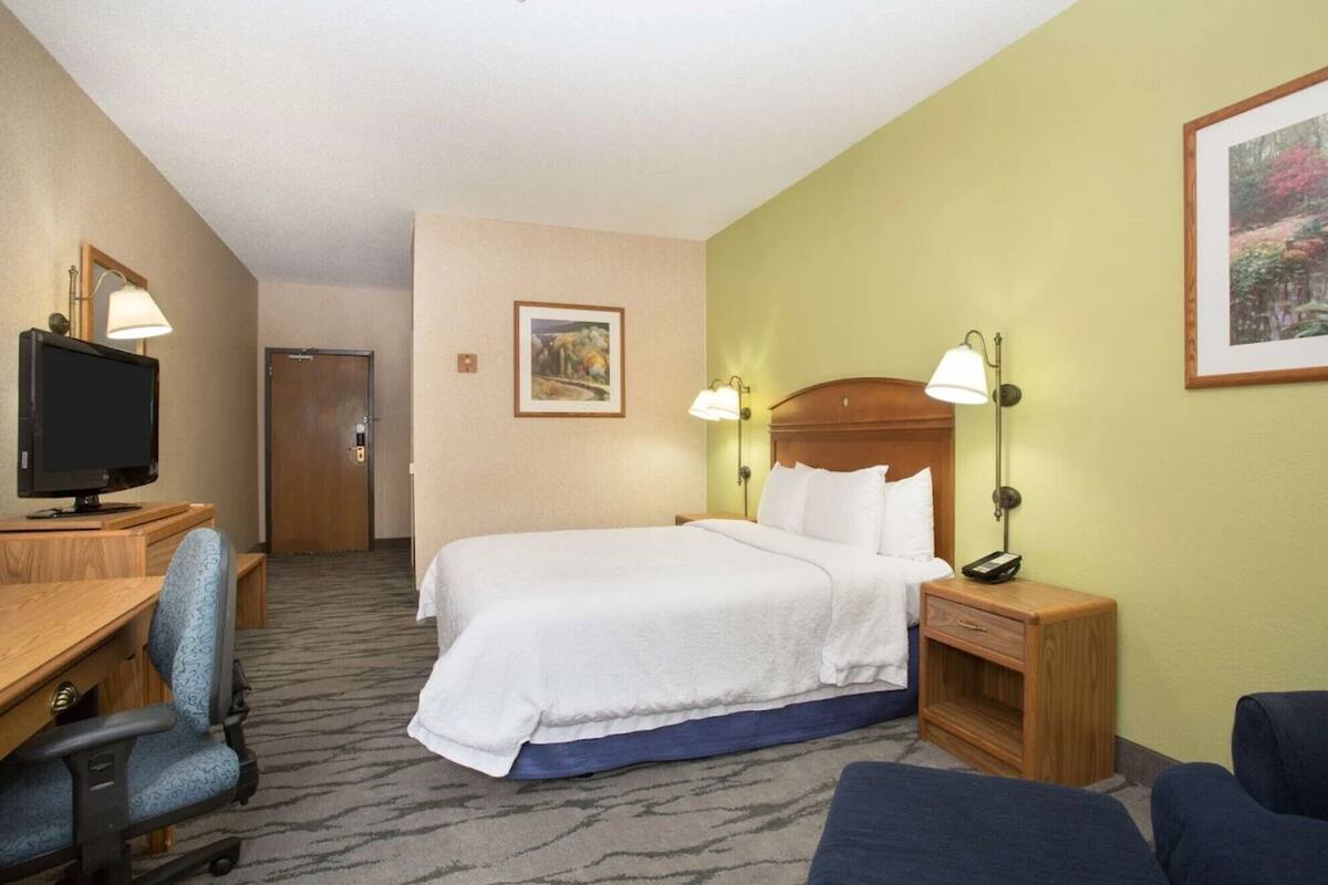 A hotel room with a bed, desk, chair, and a television.