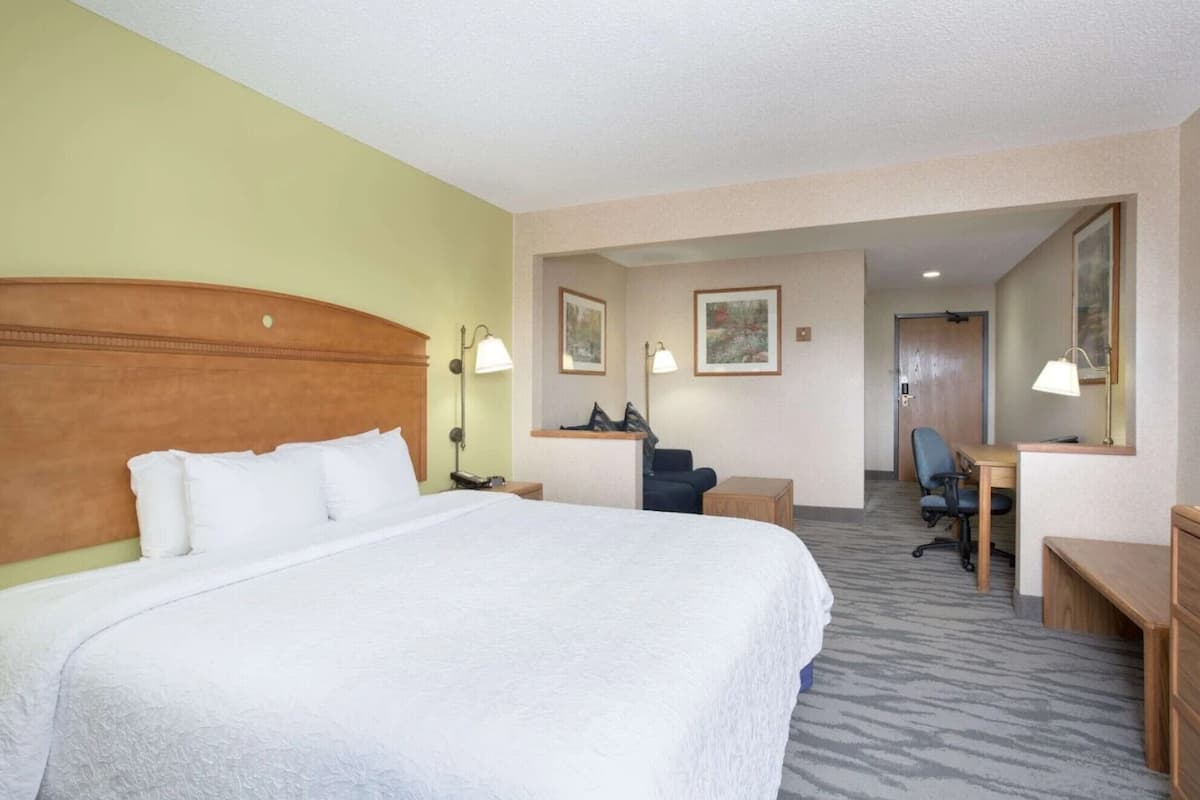 A hotel room with a large bed, a desk, a chair, and a door leading to another room.
