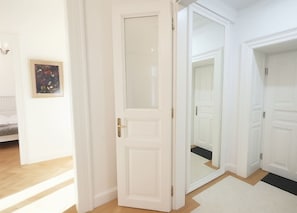 Ein Korridor mit weißen Türen, einem gerahmten Kunstwerk an der Wand und einem Holzboden.