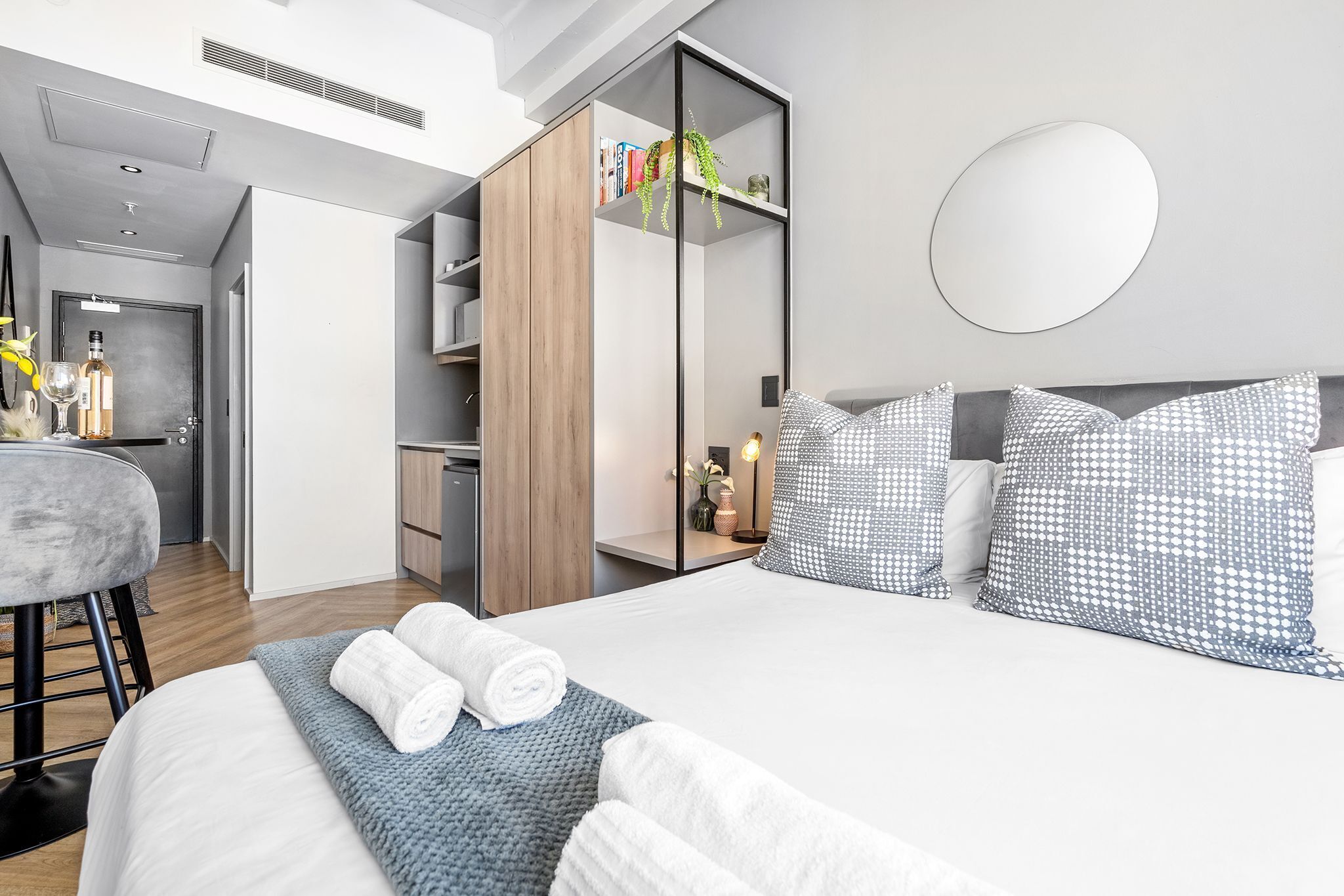 A modern hotel room with a bed, a wardrobe, a mirror, and a seating area.