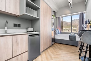 Eine moderne Küche mit Geschirrspüler, ein Essbereich mit Barhocker, ein Bett mit Blick und ein großes Fenster.