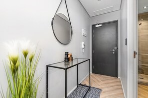 Ein Flur mit einer schwarzen Tür, einem Glastischchen, einem hängenden Spiegel und einem Blumentopf.