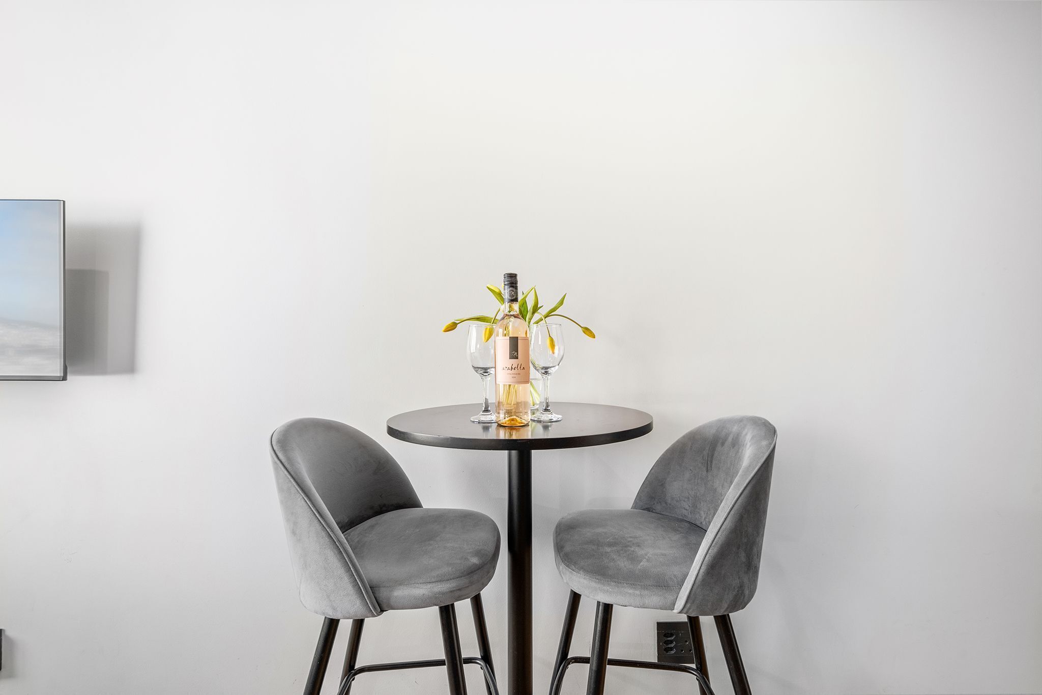 Une pièce moderne avec une table ronde, deux chaises grises à revêtement en tissu, une bouteille de champagne et deux verres.