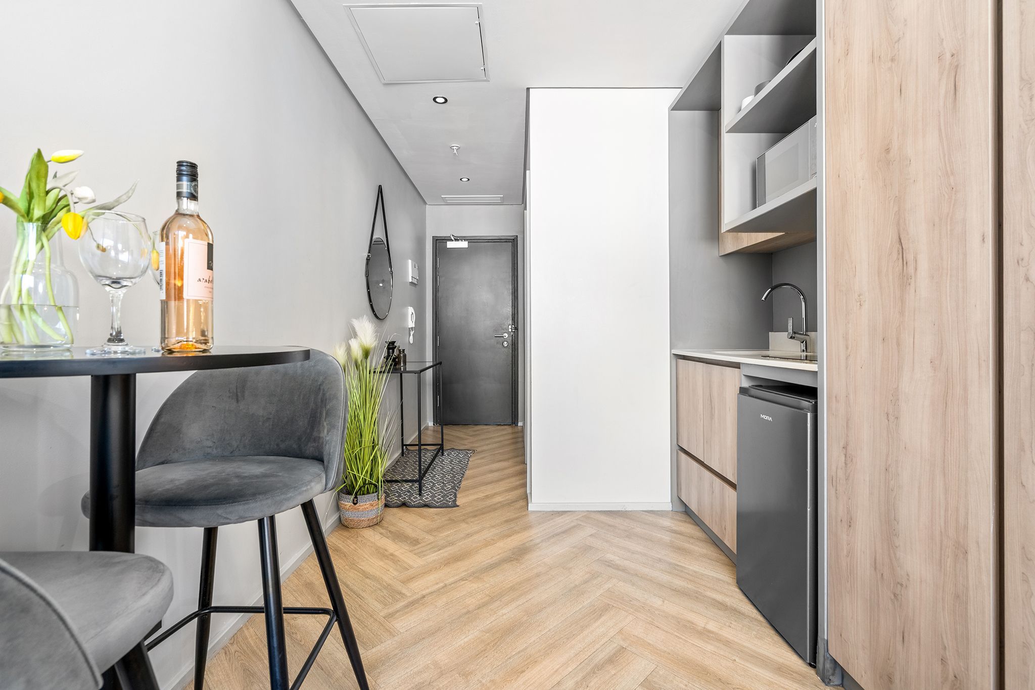 A modern kitchen with a built-in dishwasher, a dining area with a table and chairs, and a hallway leading to a door.