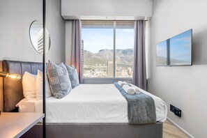 Quarto de hotel moderno com uma cama grande, televisão de tela plana, vista para a cidade e espelho na parede.