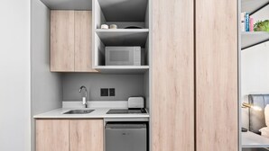 Una cocina compacta con microondas, tostadora y lavavajillas, armarios de madera y un pequeño estante con libros y una planta.