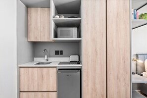 Eine kompakte Küche mit Mikrowelle, Toaster und Geschirrspüler, Holzschränken sowie einem kleinen Regal mit Büchern und einer Pflanze.