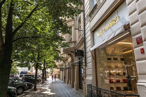 Straßenansicht mit einem Louis Vuitton Geschäft, einer von Bäumen gesäumten Fußgängerzone und geparkten Autos.
