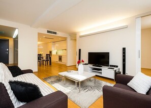A modern living room with a sofa, coffee table, TV, and a dining area in the background. - Contemporary Residence in Trendy Karlín District (Prague 8)