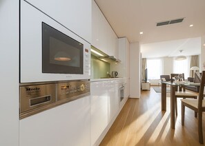 A modern kitchen with built-in appliances, a dining area with a table and chairs, and a view of the living room. - Contemporary Residence in Trendy Karlín District (Prague 8)