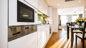 Eine moderne Küche mit integrierten Geräten, ein Essbereich mit Tisch und Stühlen sowie ein Blick ins Wohnzimmer.
