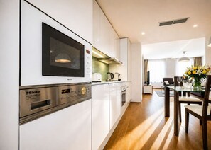 A modern kitchen with built-in appliances, a dining area with a table and chairs, and a view into the living room. - Contemporary flat in a trendy Karlin District (Prague 8)