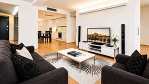 Ein modernes Wohnzimmer mit Fernseher, Couchtisch und Sofa. Im Hintergrund ist eine Küchenzeile zu sehen.
