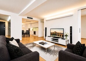 A modern living room with a flat-screen TV, a coffee table, and a sofa. There is a kitchen area in the background. - Contemporary flat in a trendy Karlin District (Prague 8)