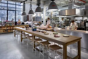 A modern kitchen with a long wooden table, bar stools, hanging pendant lights, and stainless steel appliances. - Contemporary flat in a trendy Karlin District (Prague 8)