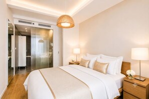 Ein Hotelzimmer mit Bett, Nachttischlampen, einem Nachttisch, Holzboden und einer Tür zu einem Badezimmer.