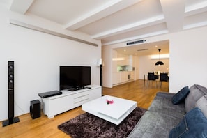 Ein modernes Wohnzimmer mit Flachbildfernseher, einer weißen Unterhaltungsanlage, einem grauen Sofa und einem Essbereich im Hintergrund.