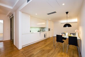 Eine moderne Küche mit weißen Schränken, eine Essecke mit schwarzen Stühlen und ein Holzboden.