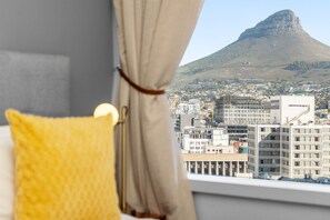 A window view of a cityscape with a prominent hill, a building with 'OceanView' signage, and a yellow pillow on a bed. - One Thibault 1609 (Cape Town)