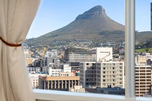 A cityscape with a prominent mountain, buildings, and a window with curtains. - One Thibault 1609 (Cape Town)
