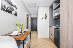 A modern kitchen with a built-in dishwasher, a dining area with a table set for two, and a hallway leading to a door. - One Thibault 1609 (Cape Town)