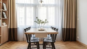 A dining area with a wooden table, black chairs, a vase with plants, and a bookshelf.